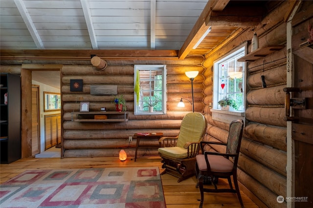 living area featuring beamed ceiling, a wealth of natural light, rustic walls, and wood-type flooring