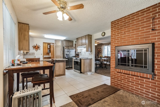 kitchen with stainless steel appliances, brick wall, ceiling fan, and light tile floors