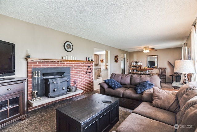 living room featuring a brick fireplace, dark carpet, ceiling fan, and a textured ceiling