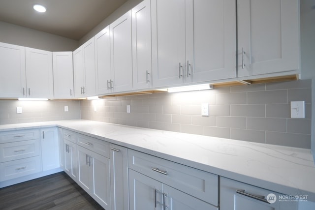 kitchen with decorative backsplash, dark hardwood / wood-style flooring, light stone counters, and white cabinetry