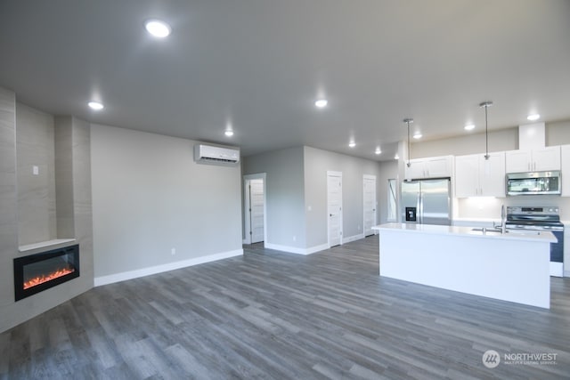 kitchen featuring appliances with stainless steel finishes, decorative light fixtures, an AC wall unit, white cabinets, and an island with sink