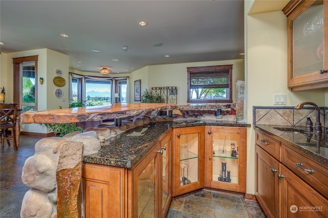 kitchen with dark stone countertops, sink, backsplash, and kitchen peninsula