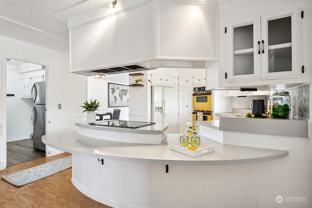 kitchen featuring stainless steel fridge, double oven, white cabinetry, light hardwood / wood-style flooring, and black electric stovetop