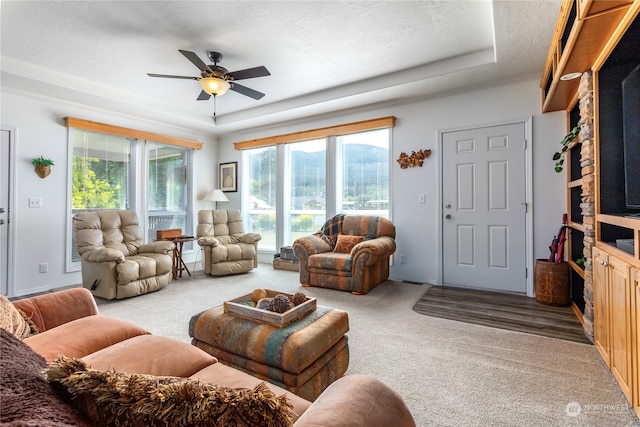 carpeted living room with ceiling fan and a raised ceiling