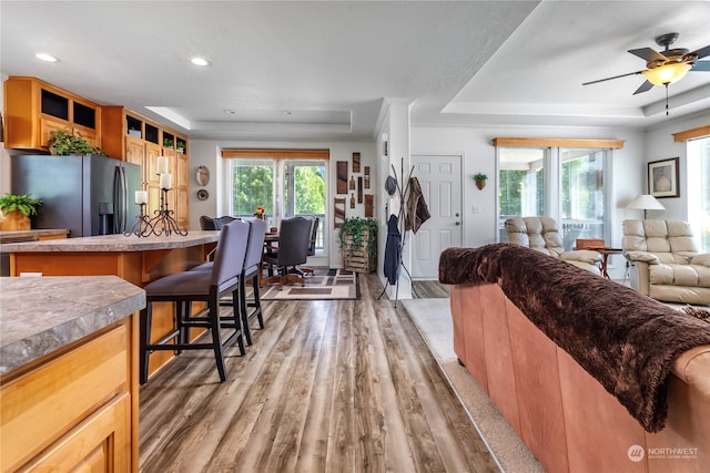 interior space featuring stainless steel fridge with ice dispenser, ceiling fan, hardwood / wood-style flooring, a raised ceiling, and a kitchen bar