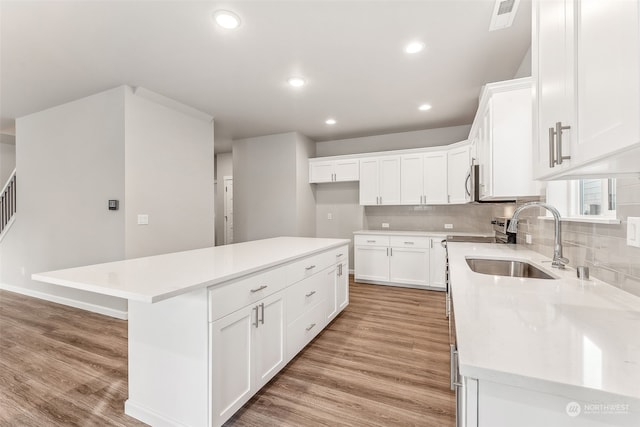 kitchen featuring light wood-type flooring, sink, a center island, and white cabinetry