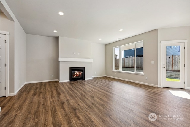 unfurnished living room with recessed lighting, baseboards, dark wood-style flooring, and a glass covered fireplace