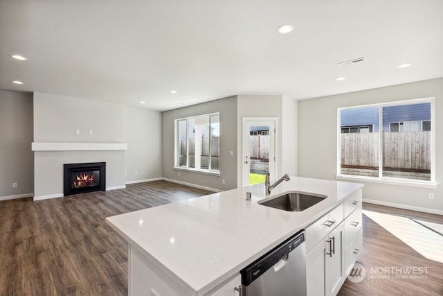 kitchen with dark wood-style floors, stainless steel dishwasher, a sink, and a center island with sink