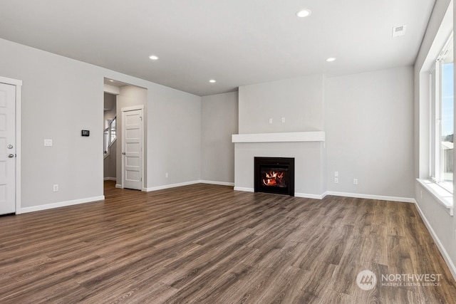 unfurnished living room with a warm lit fireplace, dark wood-style flooring, a healthy amount of sunlight, and recessed lighting