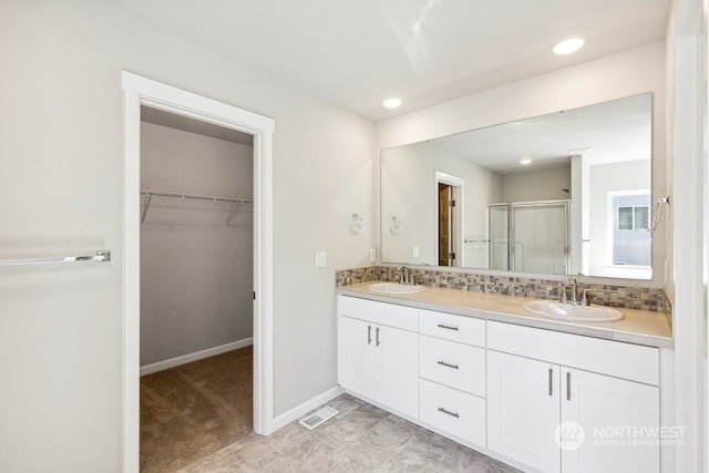 full bathroom featuring tasteful backsplash, a walk in closet, a sink, and a shower stall