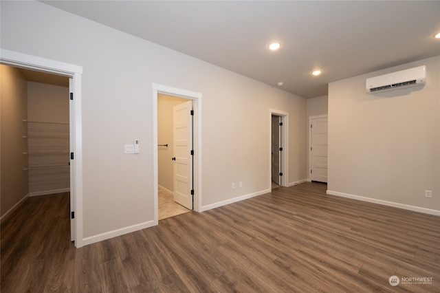 unfurnished bedroom with dark hardwood / wood-style flooring, ensuite bathroom, a spacious closet, and a wall mounted AC