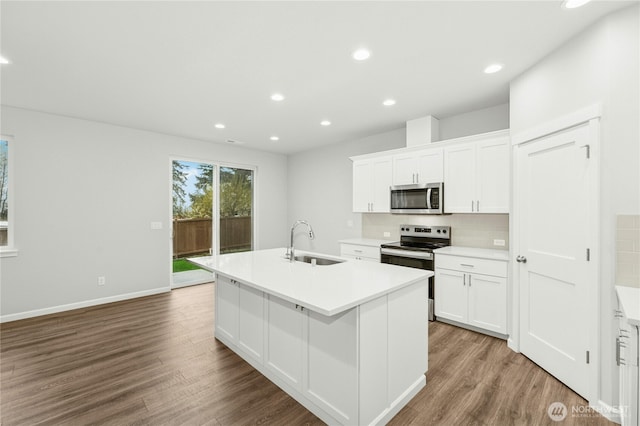 kitchen featuring stainless steel appliances, a kitchen island with sink, a sink, wood finished floors, and light countertops