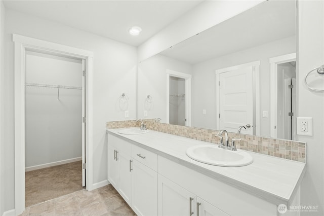 bathroom featuring a walk in closet, double vanity, baseboards, and a sink