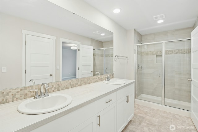 bathroom featuring double vanity, a shower stall, visible vents, and a sink