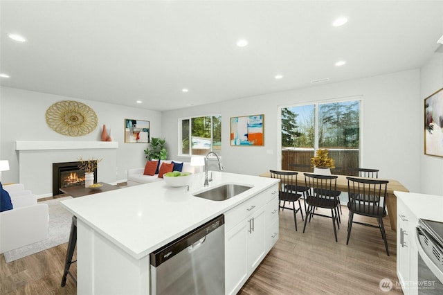 kitchen featuring a sink, light wood-type flooring, a fireplace with flush hearth, stainless steel appliances, and light countertops