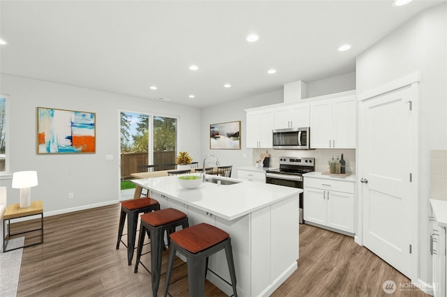 kitchen featuring an island with sink, stainless steel appliances, a breakfast bar, wood finished floors, and a sink