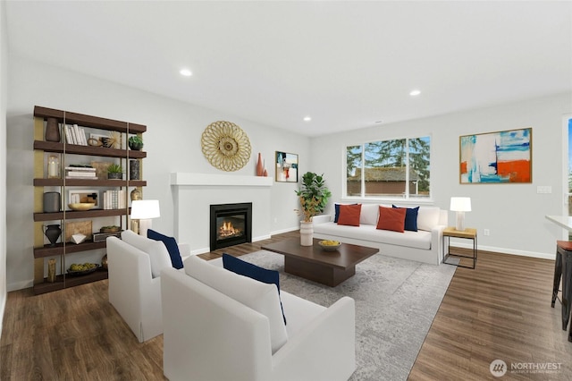 living area with a glass covered fireplace, baseboards, wood finished floors, and recessed lighting