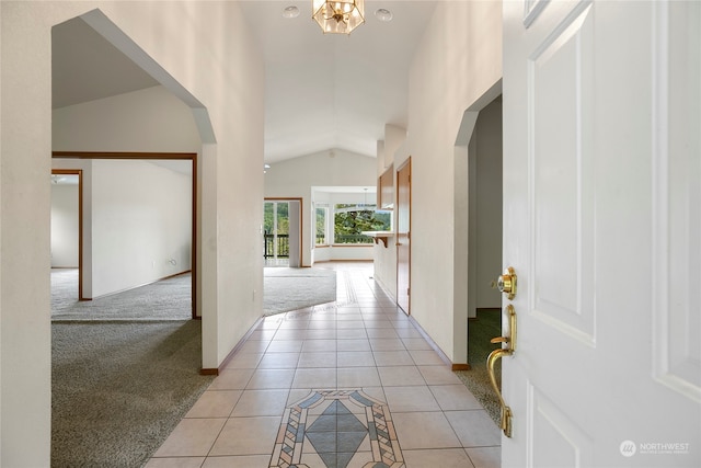 hallway featuring arched walkways, light colored carpet, lofted ceiling, and light tile patterned floors