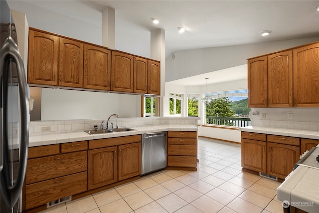 kitchen featuring appliances with stainless steel finishes, brown cabinetry, a sink, and tile counters