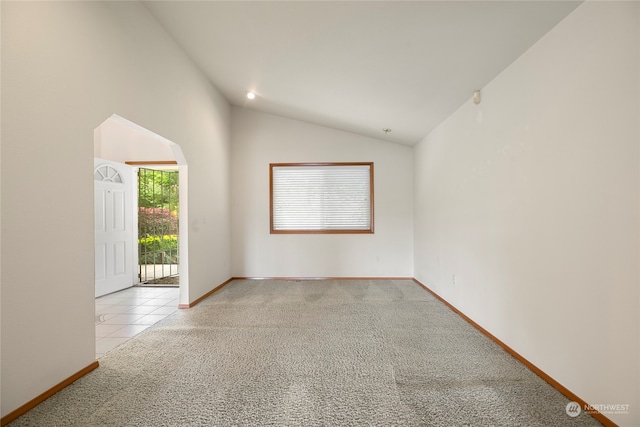 carpeted empty room featuring lofted ceiling, baseboards, arched walkways, and tile patterned floors