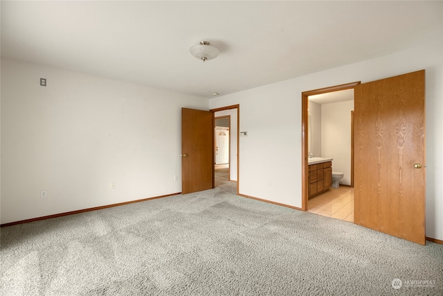 unfurnished bedroom with light colored carpet, baseboards, and ensuite bathroom