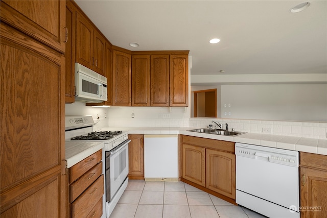 kitchen featuring white appliances, light tile patterned floors, brown cabinetry, tile countertops, and a sink