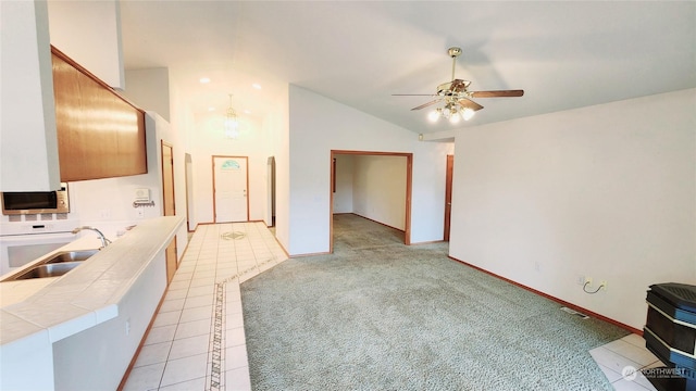 interior space featuring tile counters, stainless steel microwave, a ceiling fan, light carpet, and a sink