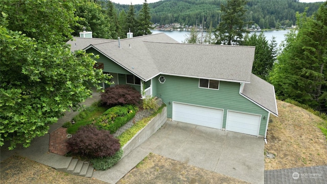 view of front of property featuring a shingled roof, concrete driveway, a water view, an attached garage, and a view of trees