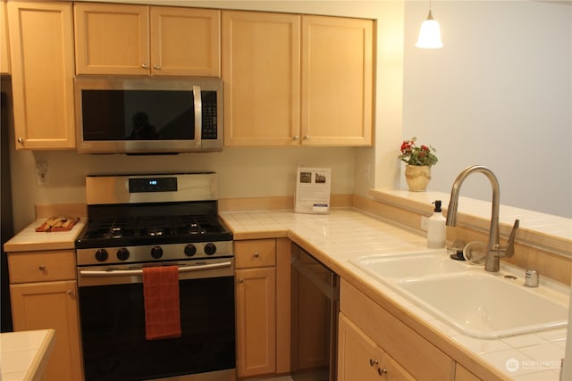 kitchen featuring hanging light fixtures, tile counters, stainless steel appliances, sink, and light brown cabinets