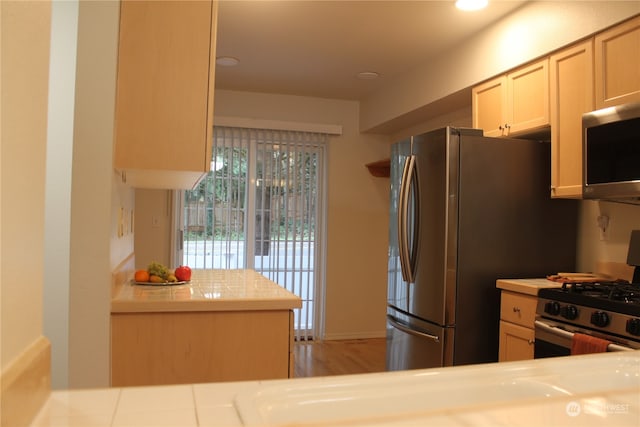 kitchen with light hardwood / wood-style flooring, kitchen peninsula, and appliances with stainless steel finishes