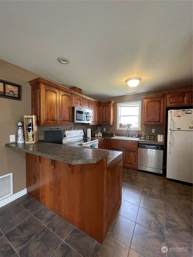 kitchen featuring appliances with stainless steel finishes, sink, dark tile floors, and kitchen peninsula