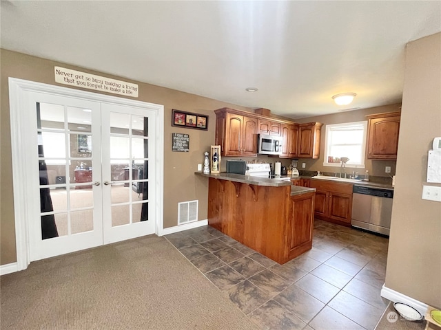 kitchen featuring french doors, stainless steel appliances, a breakfast bar area, kitchen peninsula, and dark tile flooring