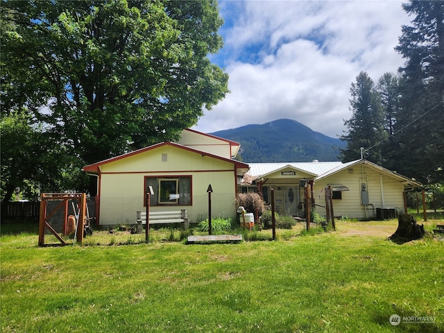 rear view of house with central air condition unit, a mountain view, fence, and a lawn