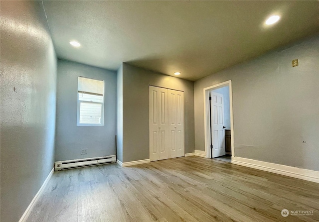 unfurnished bedroom featuring light wood-type flooring, a baseboard heating unit, and a closet