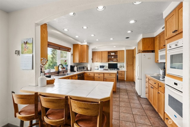 kitchen with kitchen peninsula, a breakfast bar, white appliances, sink, and light tile patterned flooring