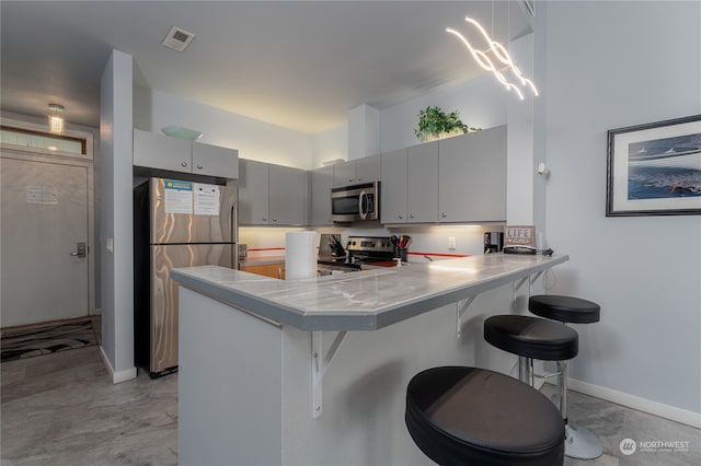 kitchen with light tile flooring, kitchen peninsula, a kitchen breakfast bar, gray cabinets, and appliances with stainless steel finishes