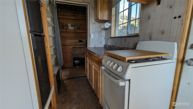 kitchen featuring dark countertops, white range with gas stovetop, brown cabinets, and wood walls