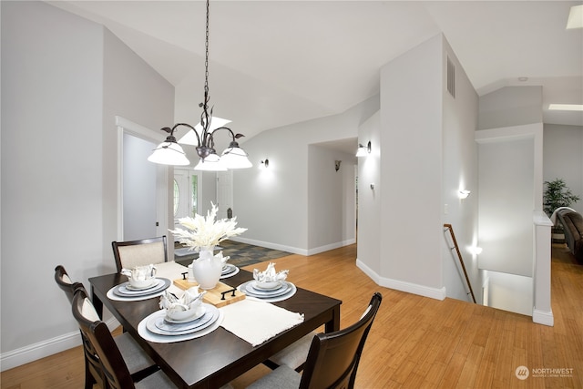 dining room with light wood-type flooring, vaulted ceiling, and an inviting chandelier