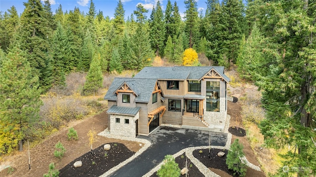 view of front of property featuring stone siding, metal roof, aphalt driveway, a standing seam roof, and a wooded view