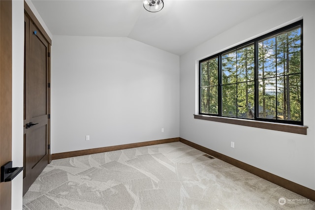 empty room featuring light carpet, baseboards, and lofted ceiling