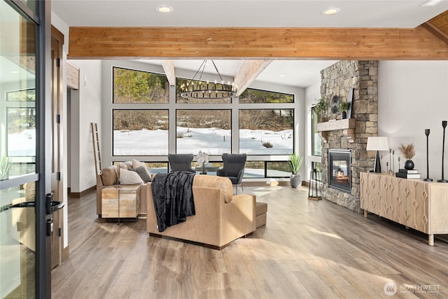 living room featuring baseboards, lofted ceiling with beams, wood finished floors, a stone fireplace, and a notable chandelier