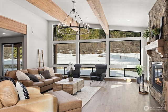 living area featuring a notable chandelier, beamed ceiling, a stone fireplace, and hardwood / wood-style floors