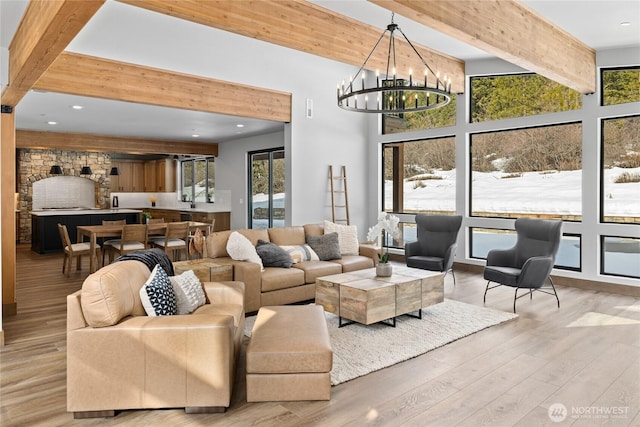 living area with beam ceiling, a notable chandelier, light wood-style flooring, and a towering ceiling