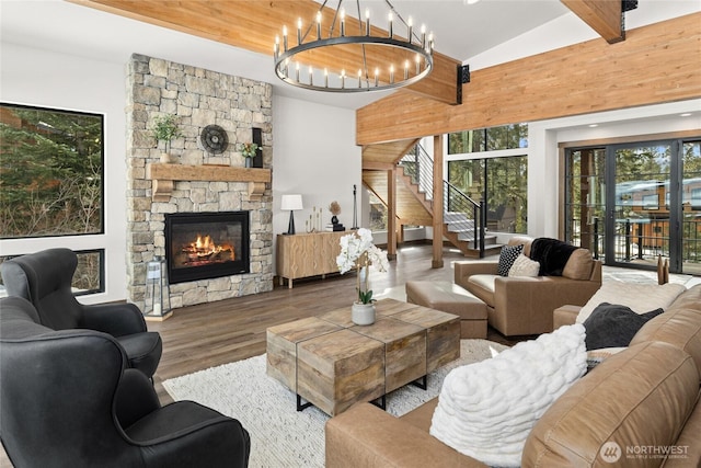 living area with stairway, wood finished floors, vaulted ceiling with beams, a stone fireplace, and a notable chandelier