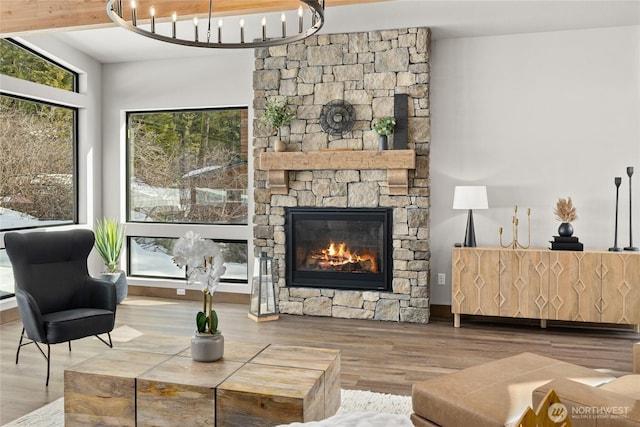 living area featuring a stone fireplace, wood finished floors, and a notable chandelier