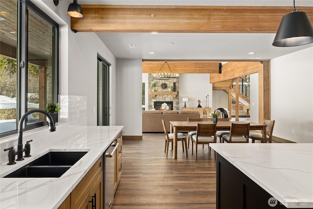 kitchen with a stone fireplace, dark wood-style flooring, a sink, hanging light fixtures, and beamed ceiling