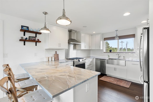 kitchen with wall chimney range hood, tasteful backsplash, a kitchen bar, appliances with stainless steel finishes, and pendant lighting