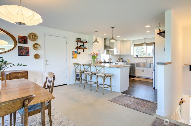 kitchen featuring a peninsula, wall chimney exhaust hood, white cabinets, a sink, and stainless steel appliances