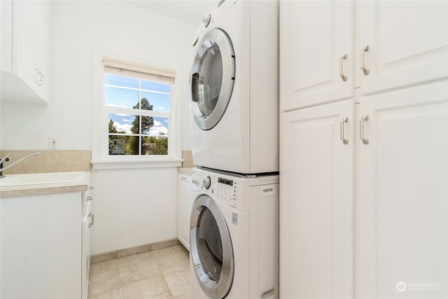 laundry area featuring cabinets, ornamental molding, stacked washer and clothes dryer, and sink