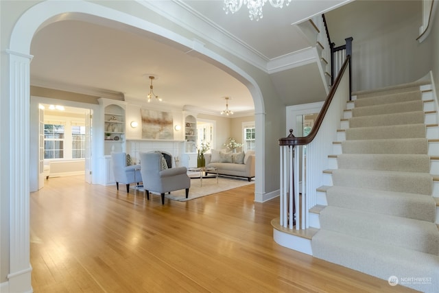 living room with an inviting chandelier, crown molding, a wealth of natural light, and light hardwood / wood-style flooring